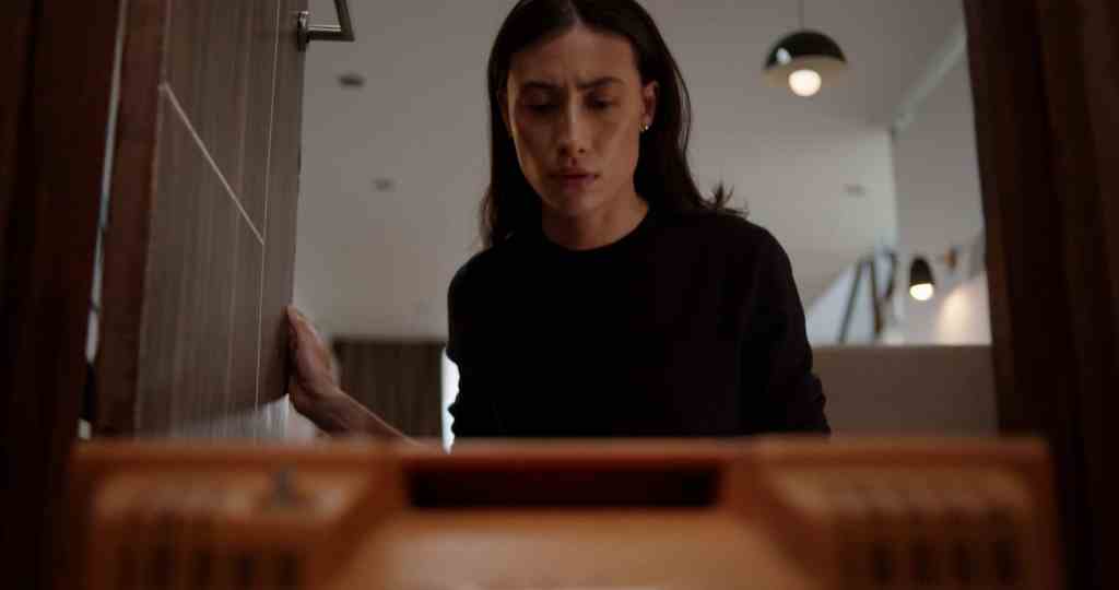 Woman peering into a dimly lit doorway, tense expression.