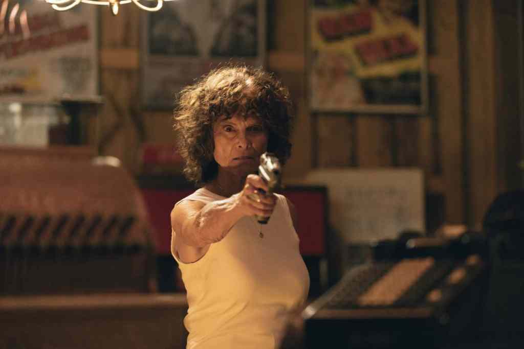 Woman with curly hair pointing a gun in a dimly lit room.