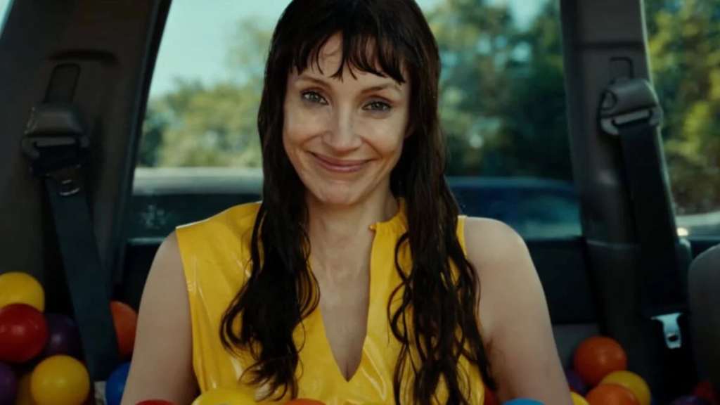 Smiling woman with dark hair in a yellow top inside a car with colorful balls in the back.