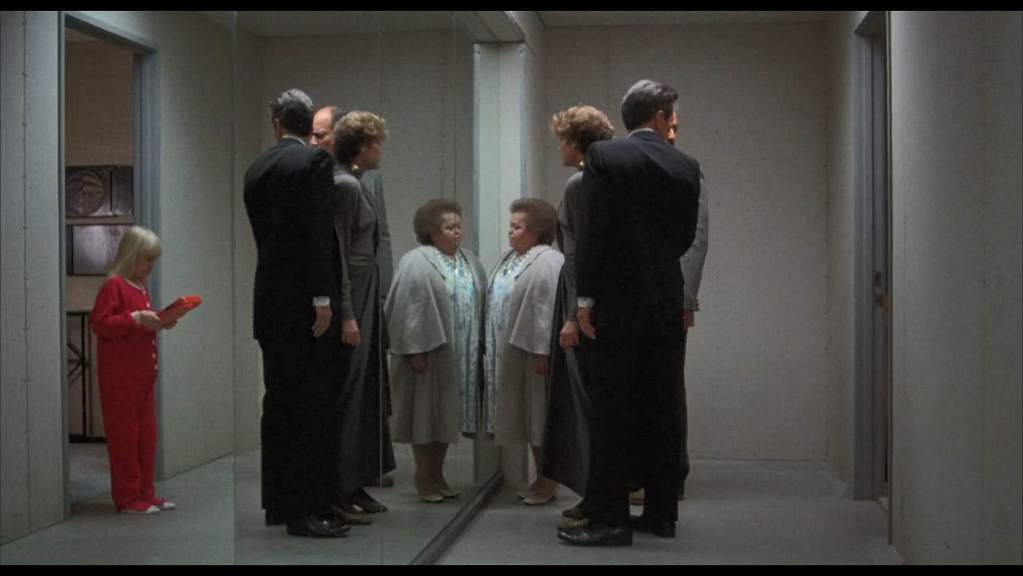 Group of people looking at their reflections in a mirror in a hallway.