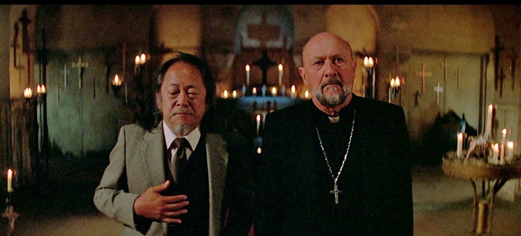 Two men in a dimly lit church with candles and crosses in the background.