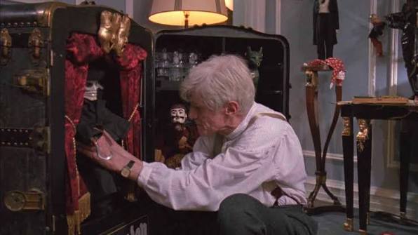 Elderly man interacting with a ventriloquist dummy in a vintage setting.