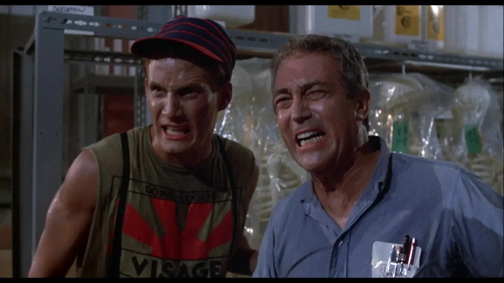 Two men with distressed expressions in a laboratory setting from a horror film scene.
