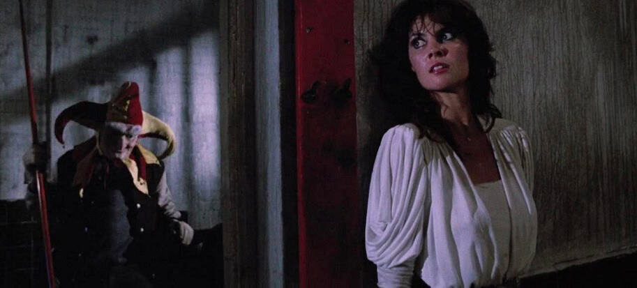Evil doll and woman in horror scene from 1980s film.