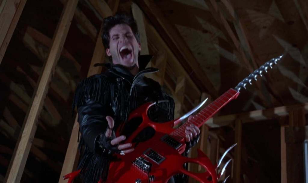 Man with a guitar in a dark, wooden attic, screaming intensely.