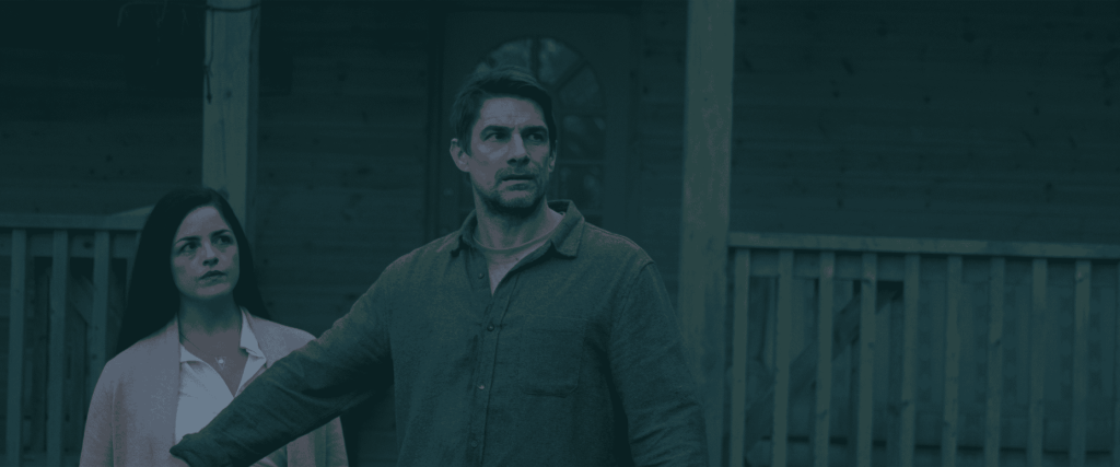 Two people outdoors near a wooden fence, serious expressions, dark lighting.