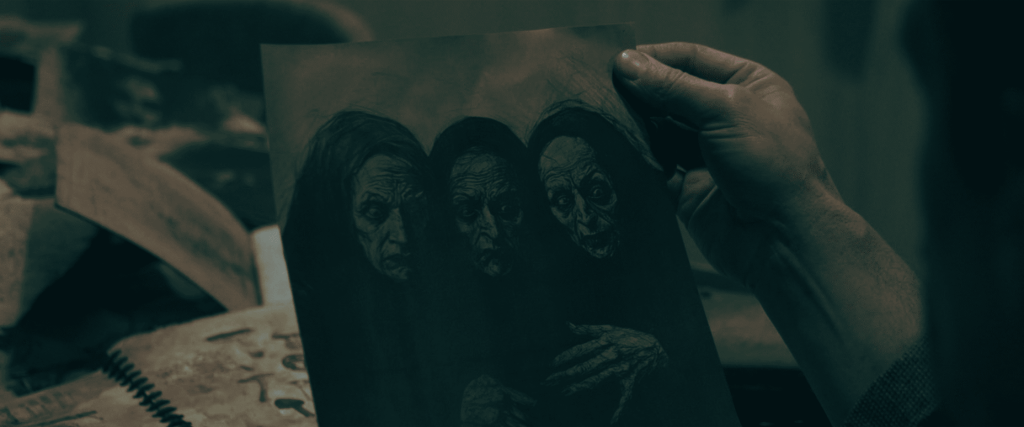 Person holding a photo of three eerie, zombie-like faces in a dimly lit room.