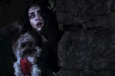 Scary woman with dark hair and a dog in a dark, rocky environment.
