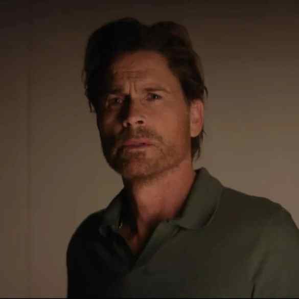 Man with brown hair and beard looking suspiciously in a dimly lit room.