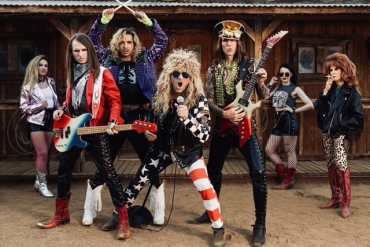 Rock band women posing with guitars and microphone outdoors in vintage setting.