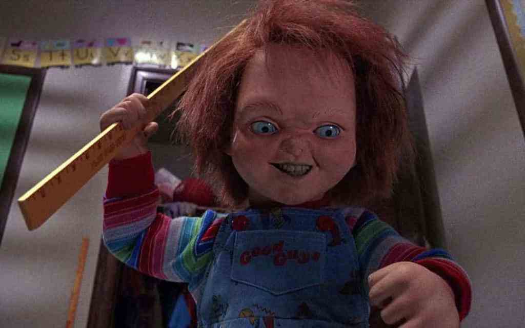 Chucky doll from Child's Play with a menacing smile and a ruler in hand.