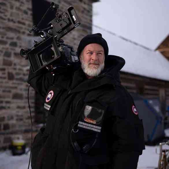 Cameraman in winter gear filming outdoors in snowy environment.